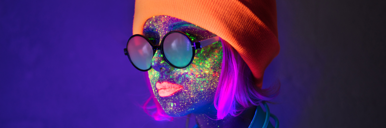 Life Lessons Autism Has Taught Me Woman in hat with fluorescent paint on lips and face and headphones.