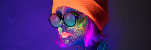 Woman in hat with fluorescent paint on lips and face and headphones.