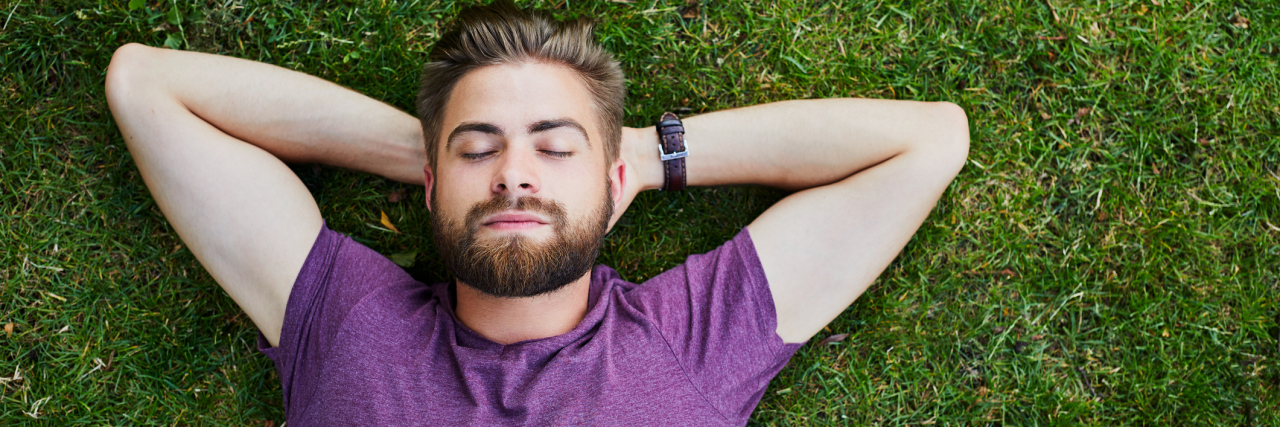 Challenging OCD Through Social Norms A man lies in the grass with his hands behind his head.