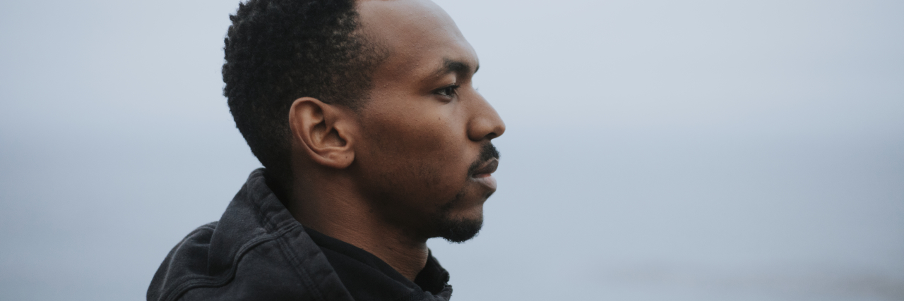 side view of a black man looking into the water wearing a black hoodie