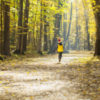 Child in a knitted hat with a pompon runs away down the path in the autumn park on a sunny day.