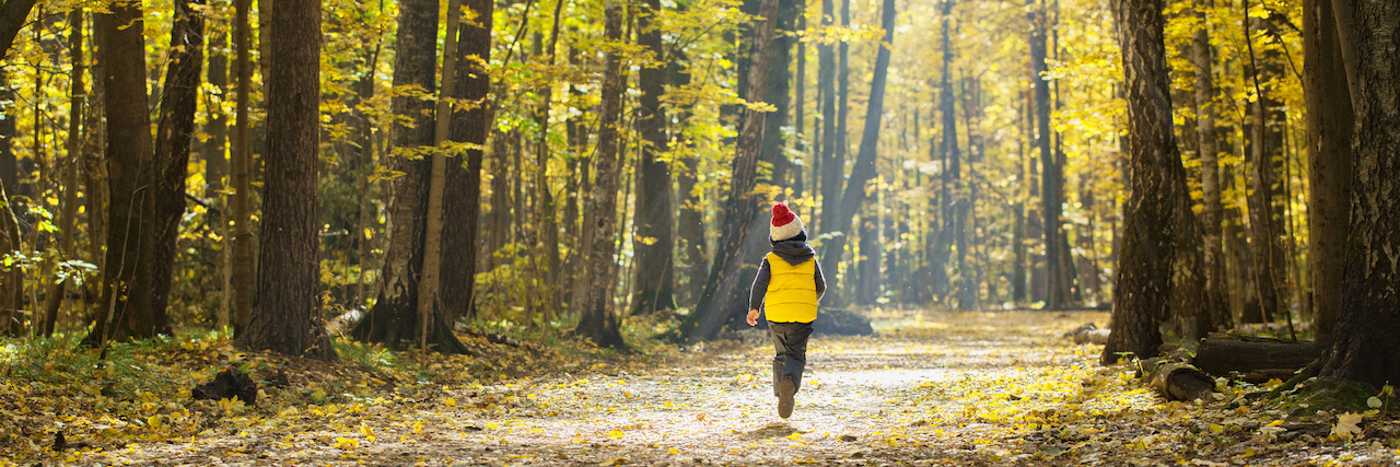 What I Wish My Parents Understood About My Life With Chronic Illness Child in a knitted hat with a pompon runs away down the path in the autumn park on a sunny day.
