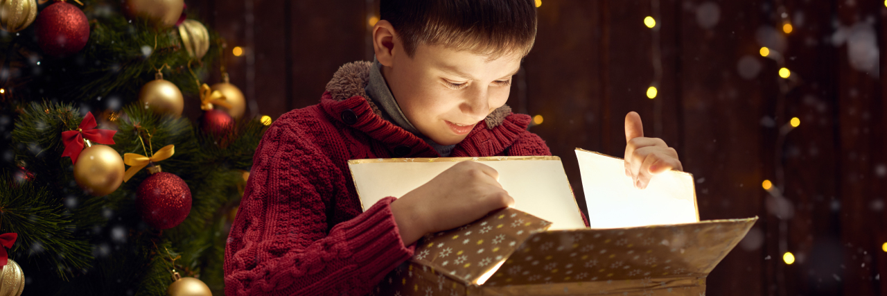 Boy looking in box with Christmas tree in the background.