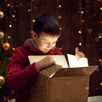 Boy looking in box with Christmas tree in the background.