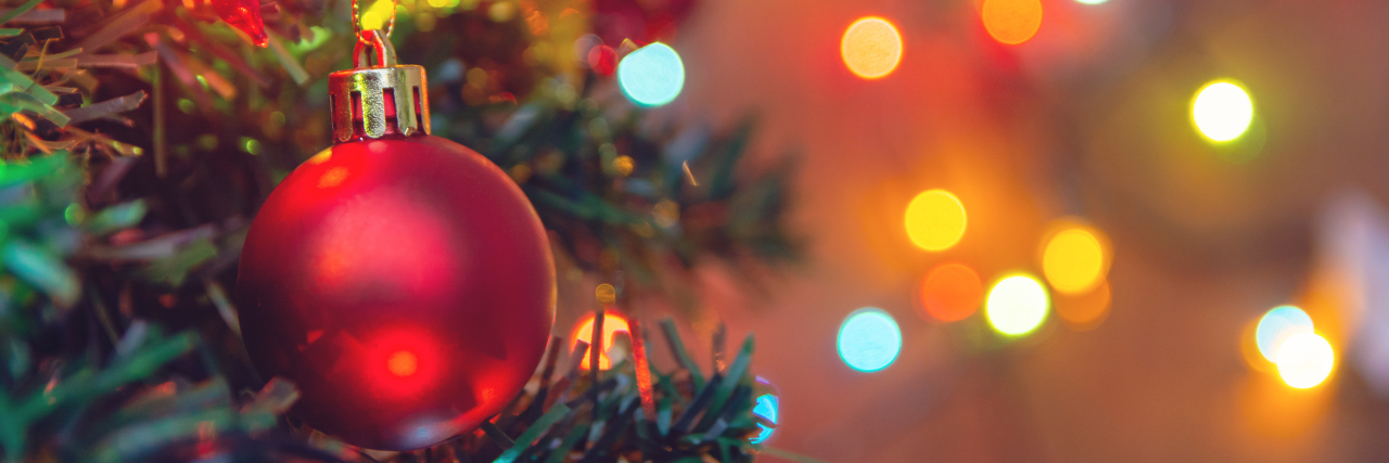 How to Survive the Holidays With Chronic Illness Christmas decoration. Hanging red ball on pine branches.