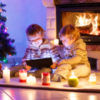 Two young boys looking at a tablet by a fireplace and Christmas tree.
