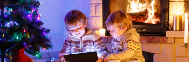 Two young boys looking at a tablet by a fireplace and Christmas tree.