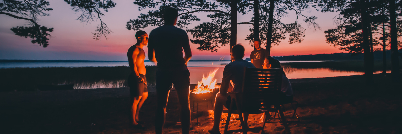 21 Things Working at a Summer Camp Taught Me About Mental Health group of people sitting and standing around a campfire with a lake in the background at a sunset