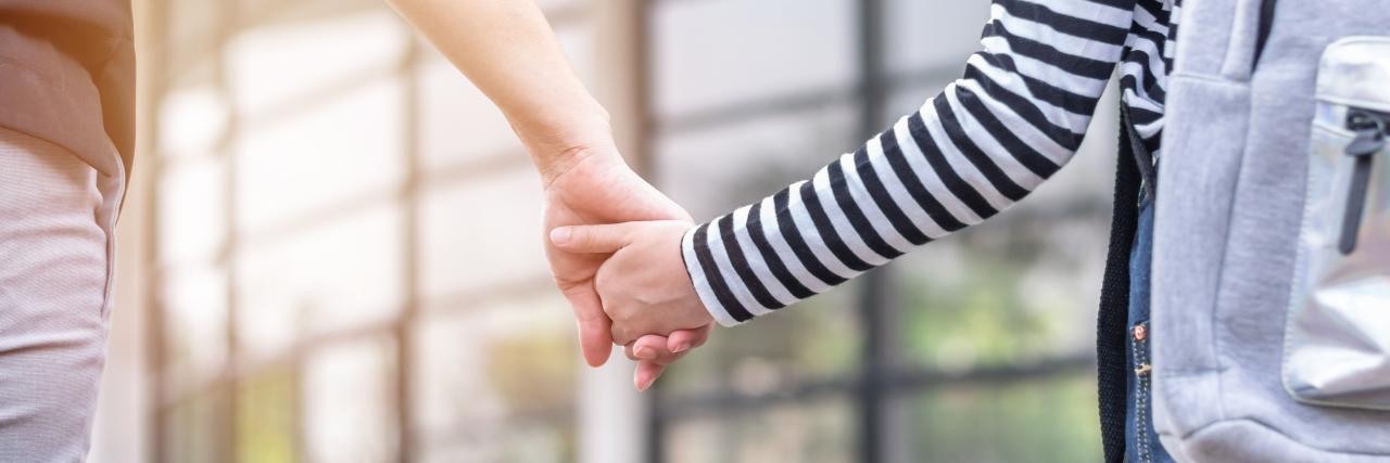 Educators Need to Show More Understanding Towards Kids Living With a Rare Disease Parent holding child's hand in front of a school