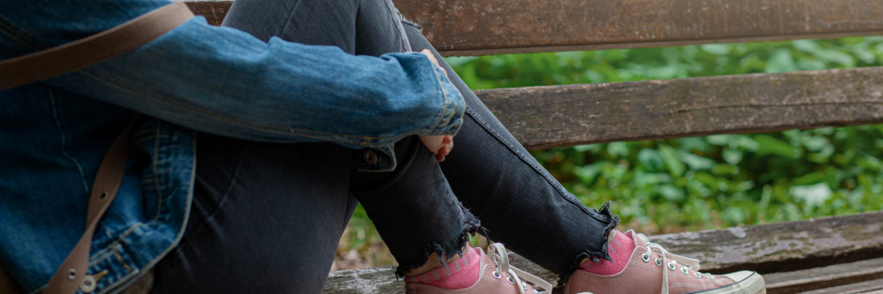 The Struggle of Coming to Terms With Having an Illness Since Childhood blonde woman in jeans sitting on park bench