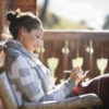 woman sitting outside on a cabin porch in a grey and white sweater writing