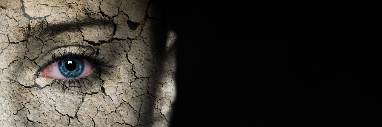Woman's face covered with cracked earth texture.