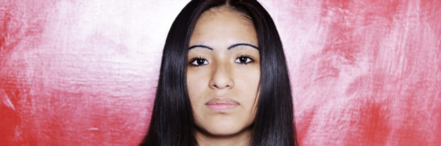 hispanic woman with serious face and long, straight black hair staring at camera with a red background