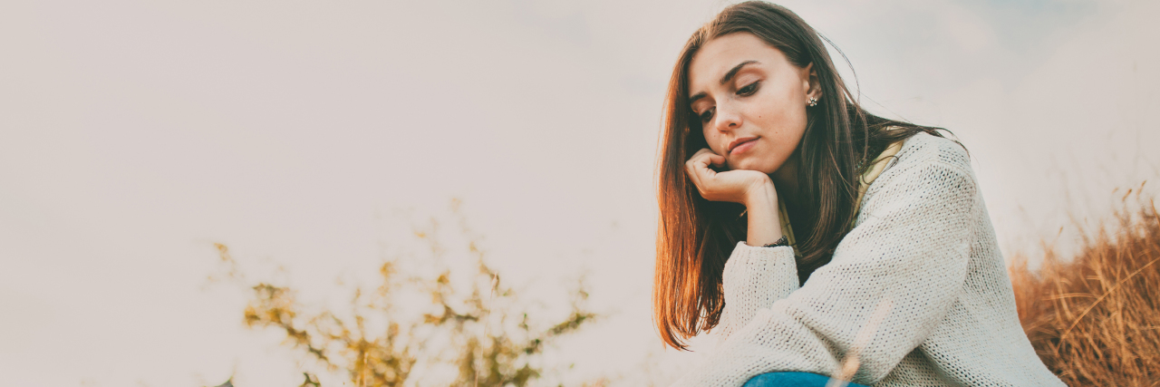 Starting a New Life With Anorexia Nervosa A woman sits alone in the grass contemplating.