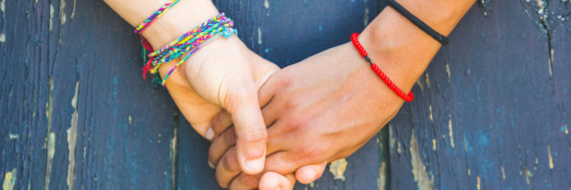 Two friends holding hands in front of a wooden background.