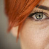 close up shot of a woman's green eye looking at the camera with red haired bangs over her face