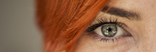 close up shot of a woman's green eye looking at the camera with red haired bangs over her face