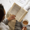 Woman reading book in bed and drinking coffee.