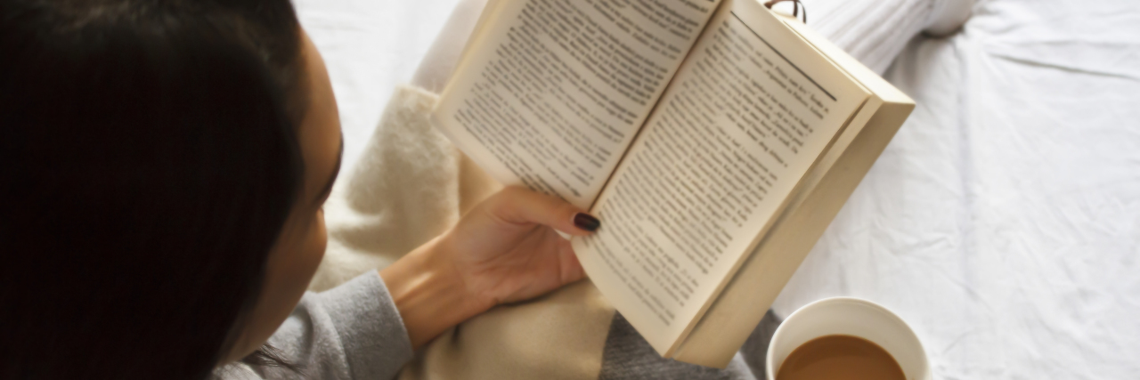 9 Best Books About Life With Chronic Illness Woman reading book in bed and drinking coffee.