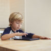 Young boy using tablet computer at kitchen table.