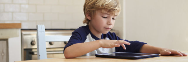 Young boy using tablet computer at kitchen table.