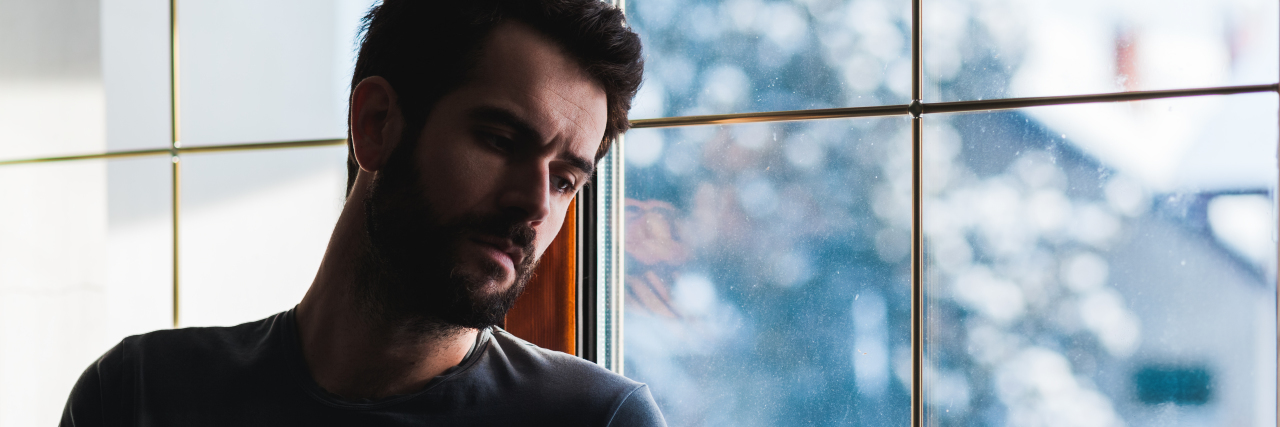 5 Ways to Manage Grief During the Holidays Instead of Repressing It young man standing against the window sad, snowing outside