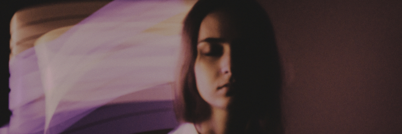 How Being Bipolar Affects My Life A photo of a woman standing with her eyes closed in front of an abstract background.