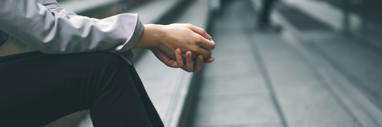 When My Boss Ignored the Limitations My Panic Disorder Forced photo of a businesswoman in black pants and a long sleeve shirt sitting on stairs with her hands together