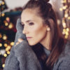 woman in oversized gray sweater with brown hair looking to the side with a Christmas tree in the background