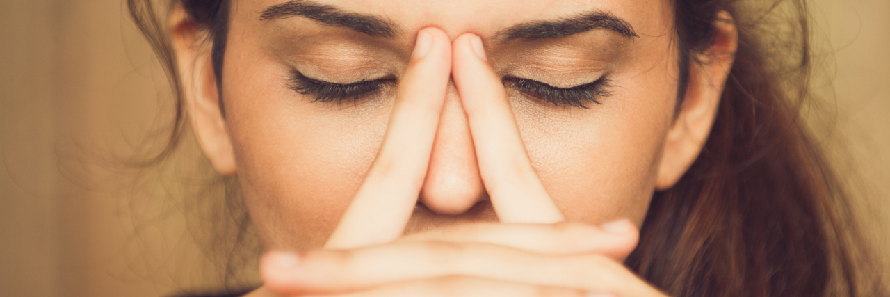Helping to Manage Depression Through Self-Care A woman sits with her eyes closed with her fingers rubbing her nose.