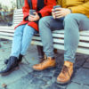 photo of 2 people sitting on a bench in fall clothes with coffee in their hands