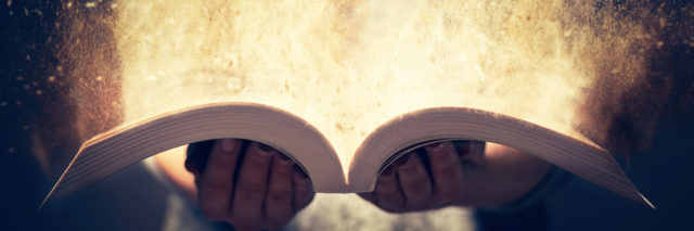 Woman holding an open book with two hands. Light coming out of the book