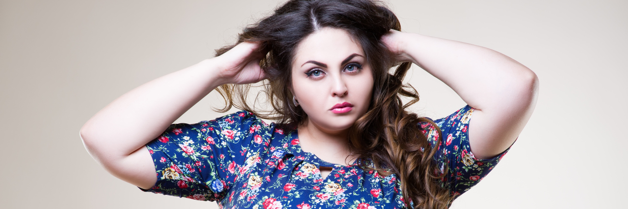 What It Looks Like for Me to Accept My Bipolar Disorder woman with long brown hair and a blue flowered dress looking seriously at the camera with her hands in her hair