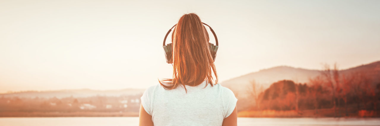 Back to Brain Injury Basics Woman meditating with headphones by the water.