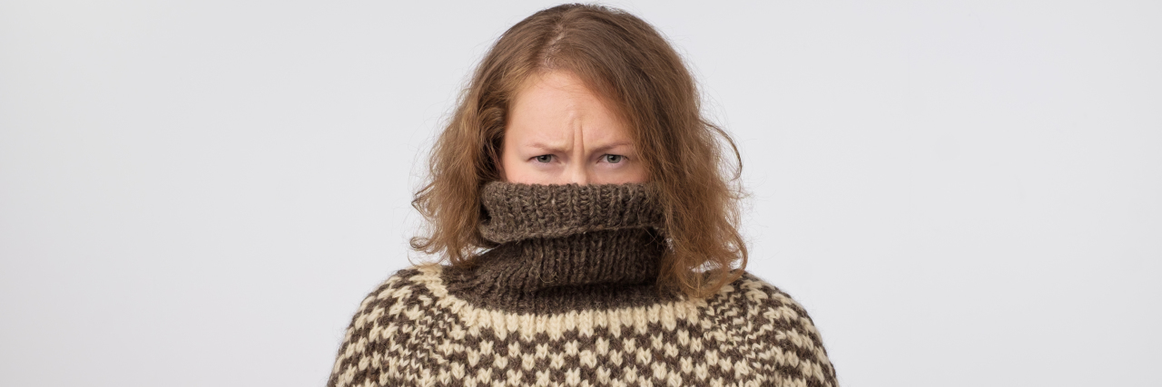woman in brown and pale turtleneck with her face buried in the sweater looking at the camera
