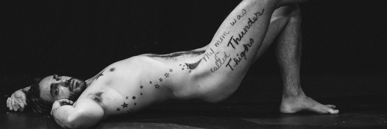 How This Body Positivity Photo Project Changed Me photo of man in black and white, lying nude with one leg raised. on his leg is written "my mom was called thunder thighs"
