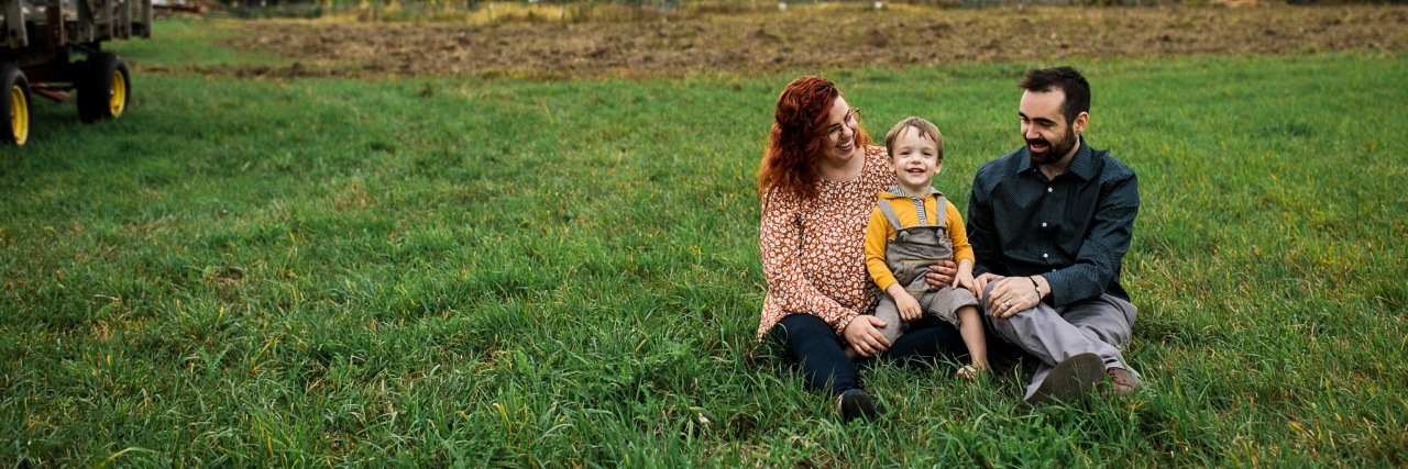 parents sitting with their son in a green field of grass