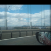 A scenic photo of a car driving over a bridge with clouds in the background.