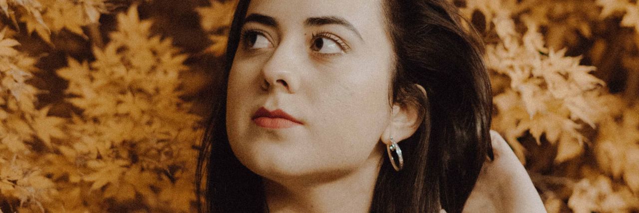 When Family Think My Depression Is Cured Over the Holidays photo of woman with dark hair standing in front of autumn leaves with hand in her hair