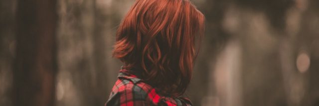 side view of woman with red hair in a red and black flannel shirt looking straight ahead in a forest