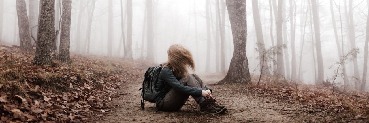 What I Remind Myself of on My Bad Mental Health Days artsy shot of a woman sitting in the forest with her hair blocking her face in the transition from fall to winter