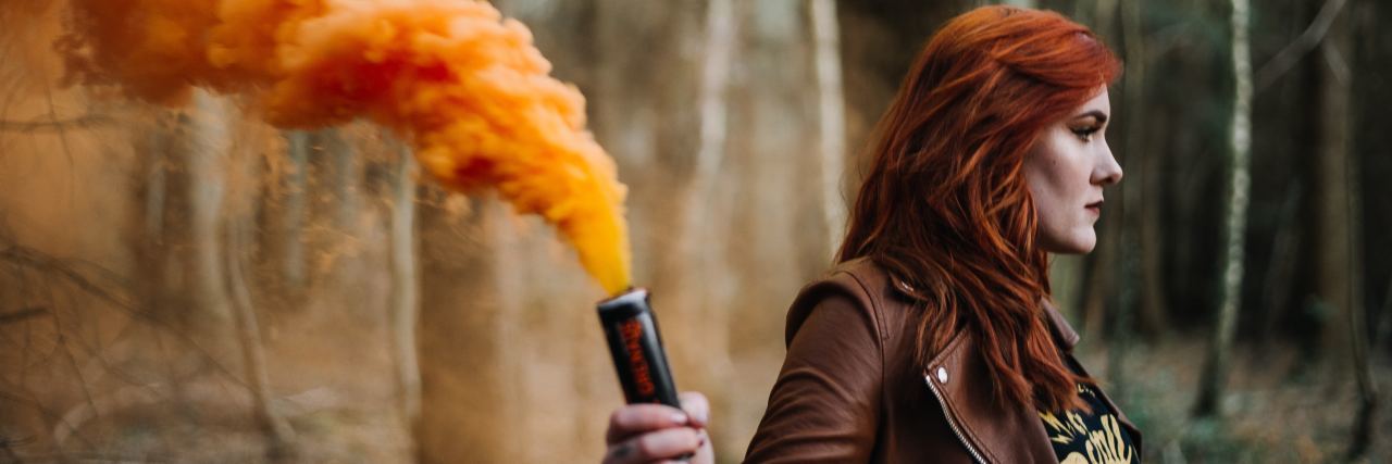 Why I'm Wearing My 'Borderline Personality Disorder' Label With Pride photo of redhead woman in forest holding smoke canister and orange smoke