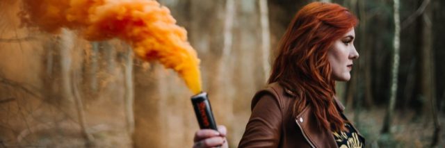 photo of redhead woman in forest holding smoke canister and orange smoke