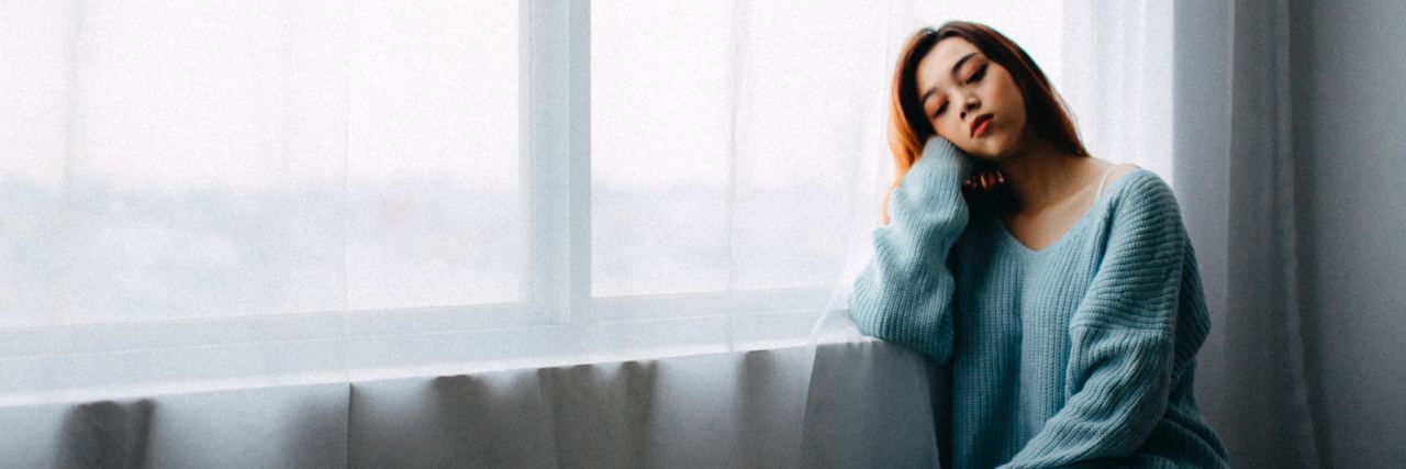 When My Sense of Relief Faded Into Grief After My Child's Rare Diagnosis Woman looking outside a window, sitting on the floor