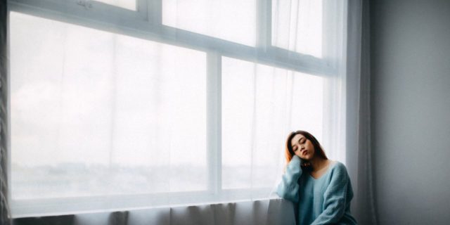 Woman looking outside a window, sitting on the floor