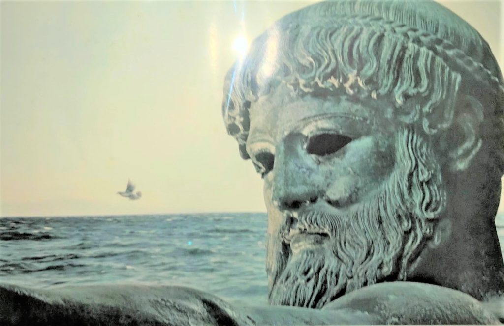 photo of a photograph showing a statue of poseidon beside the ocean, a light glare on his forehead