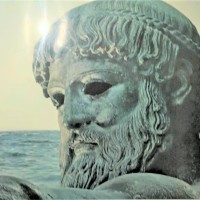 photo of a photograph showing a statue of poseidon beside the ocean, a light glare on his forehead