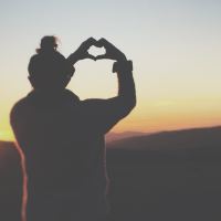 photo of woman silhouetted against sunset making heart shape with hands