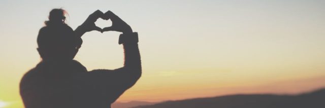 photo of woman silhouetted against sunset making heart shape with hands