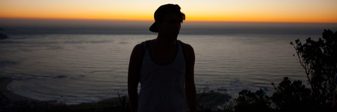 KHN: Why Mental Illness Increases Immigrant Risk of Deportation Silhouette of a man against a body of water at sunset